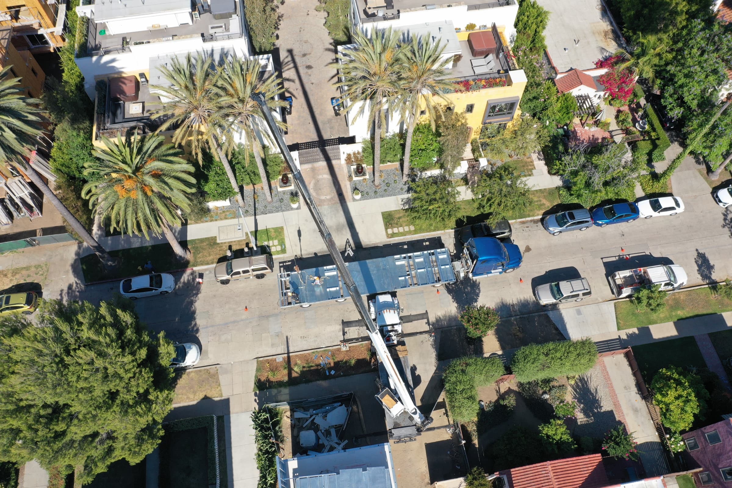 Aerial of a LyteMods delivery, a boom truck craning factory-built steel panels off a flatbed onto a home site on a tree-lined street