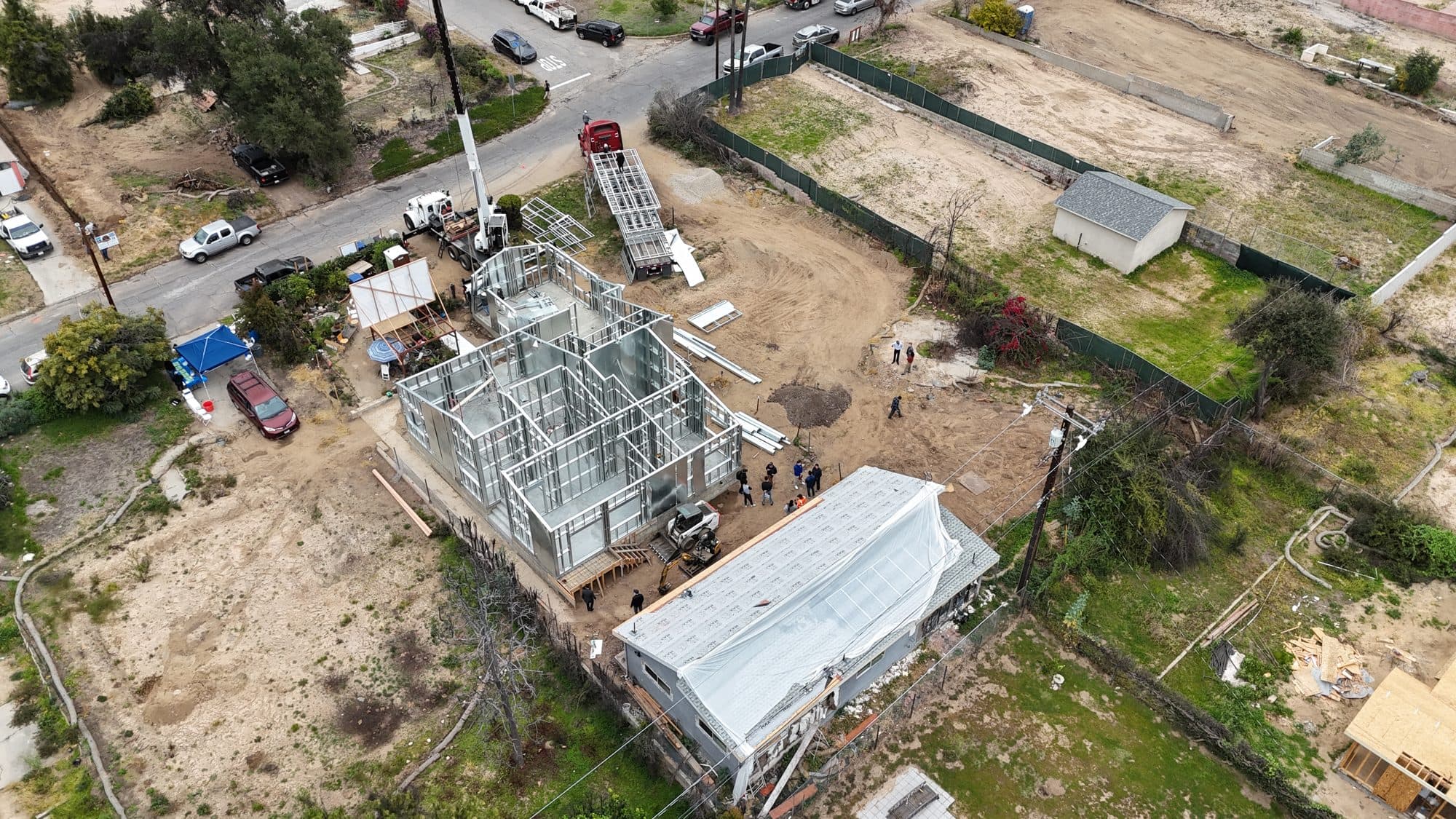Aerial view of a light-gauge steel home frame assembled on its lot as panels are craned into place