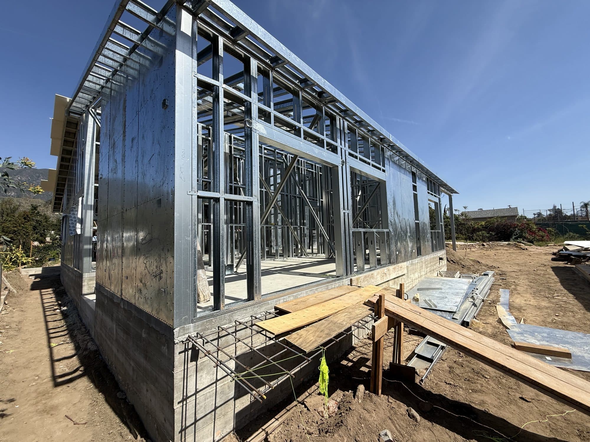 Ground-level view of the 480 W Palm light-gauge steel frame standing on its foundation against the San Gabriel mountains