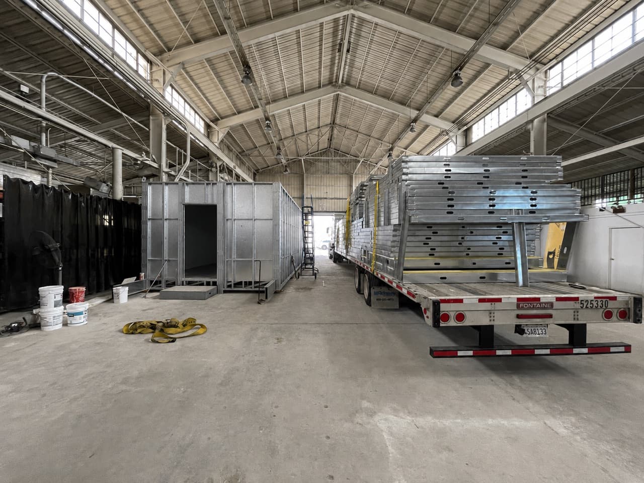 Inside the factory: a complete volumetric light-gauge steel module on the left, and a flatbed stacked with flat panelized steel wall panels on the right